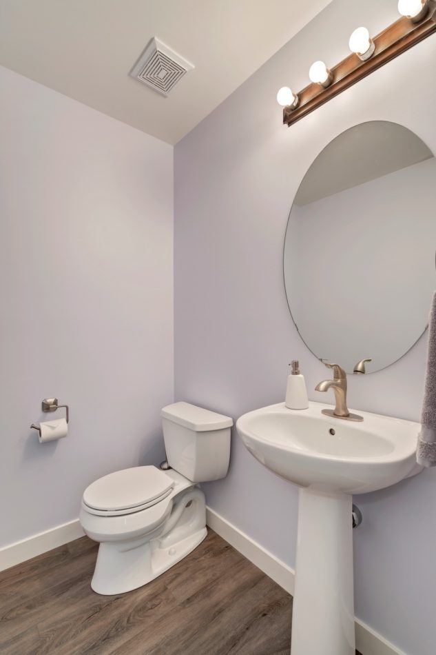 A small half-bath with a unique pedestal sink and round mirror