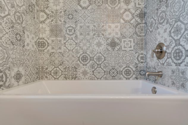 A beautiful grey and white tile mosaic surrounds a large tub in this master ensuite