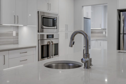 Modern high gloss kitchen cabinetry with grey quartz countertops and exposed steel beam