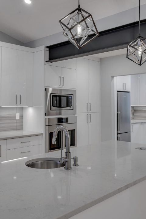Modern high gloss kitchen cabinetry with grey quartz countertops and exposed steel beam