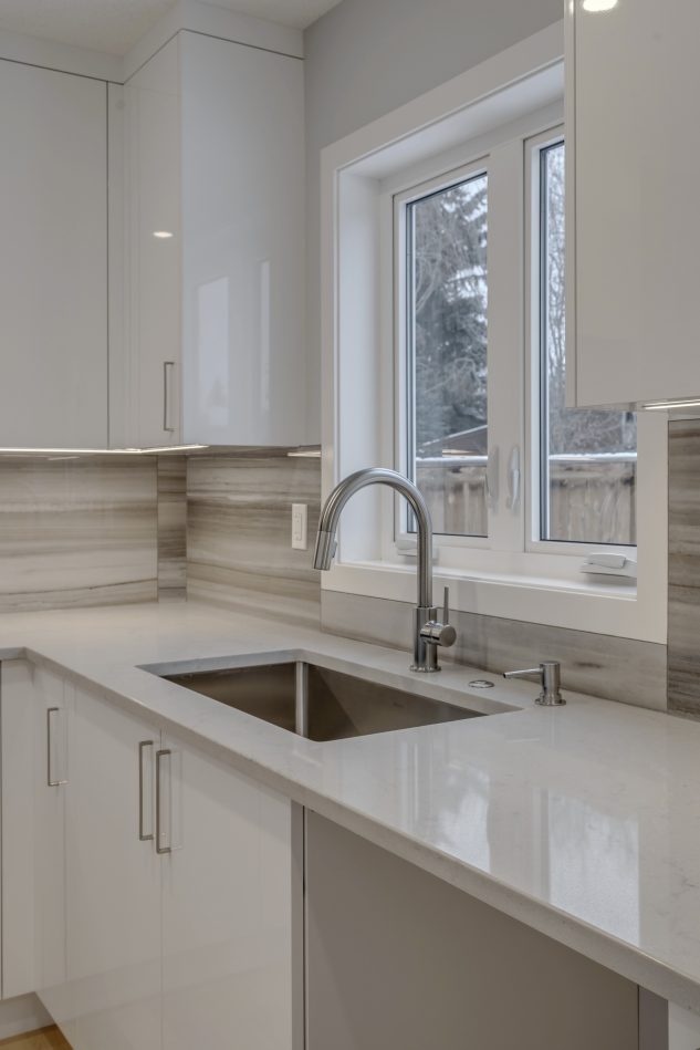 Modern high gloss kitchen cabinetry with grey quartz countertops. Scullery kitchen with stainless steel sink. 