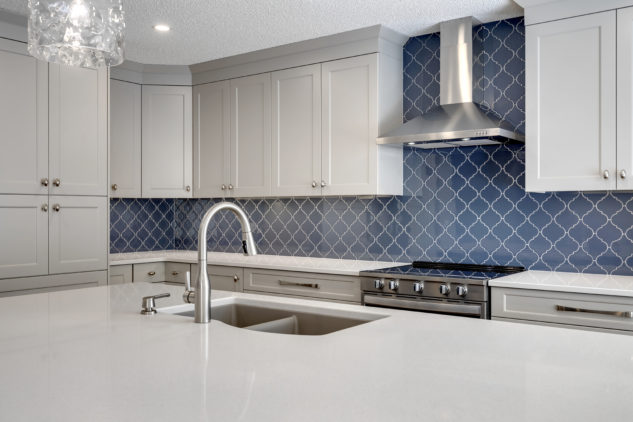 kitchen with large blue island and custom cabinetry. Blue Arabesque tiled backsplash with stainless steel hood fan 