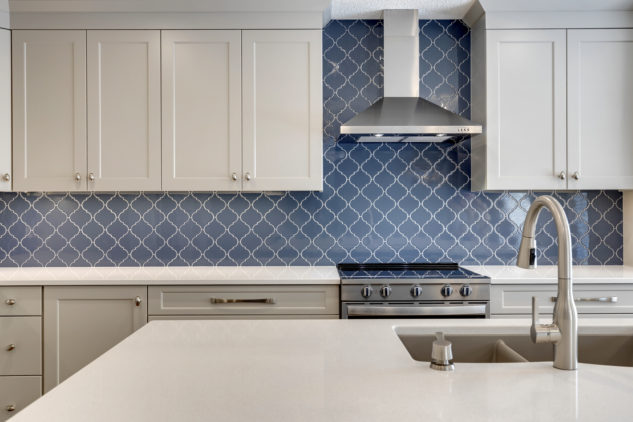 kitchen with large blue island and custom cabinetry. Blue Arabesque tiled backsplash with stainless steel hood fan 