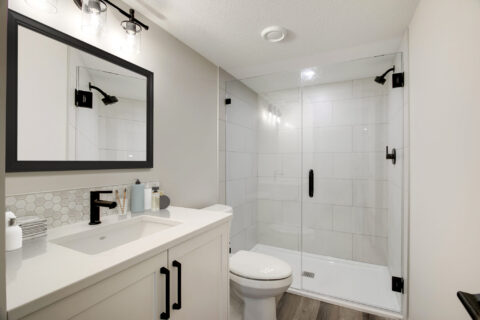 Ensuite with white cabinetry and tiled shower. Black handles and bath accessories