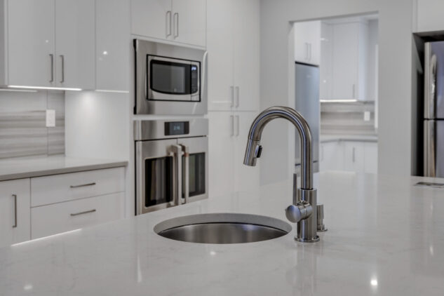 Modern high gloss kitchen cabinetry with grey quartz countertops and exposed steel beam