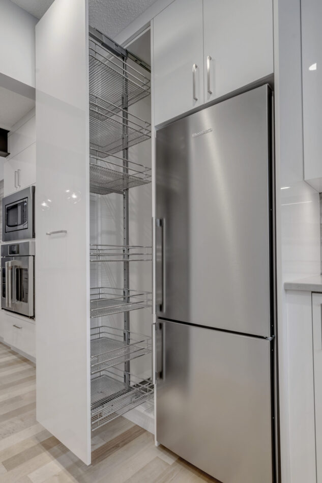 Modern high gloss kitchen cabinetry with grey quartz countertops. Cabinet accessory pull out next to stainless steel fridge.