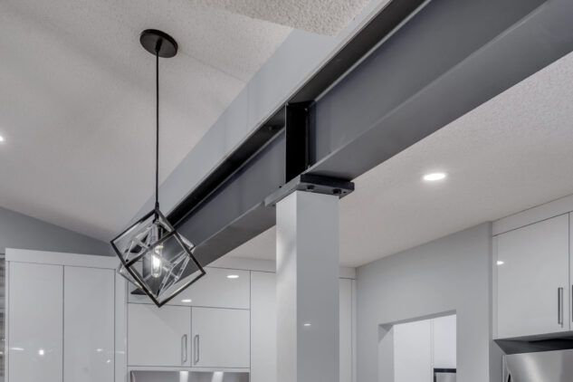 Modern high gloss kitchen cabinetry with grey quartz countertops and exposed steel beam