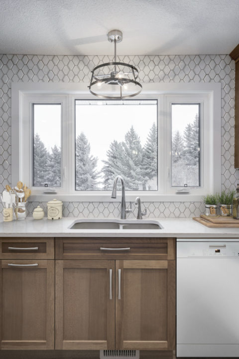 Maple stained cabinetry, white quartz countertops and tiled backsplash surrounding a window.