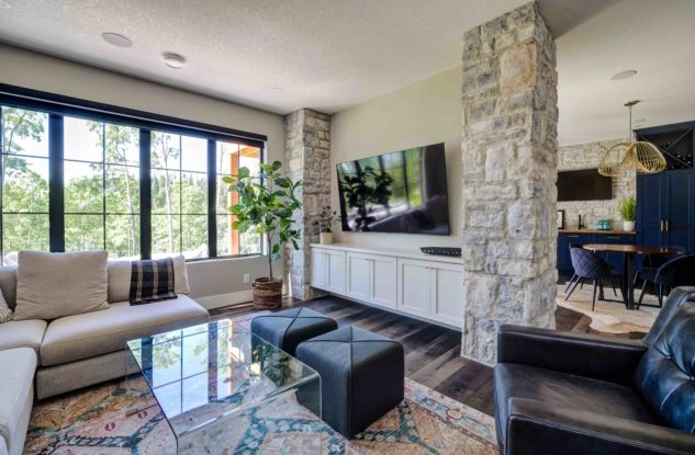 Basement living room with large black aluminum clad windows featuring stone columns a built-in storage unit
