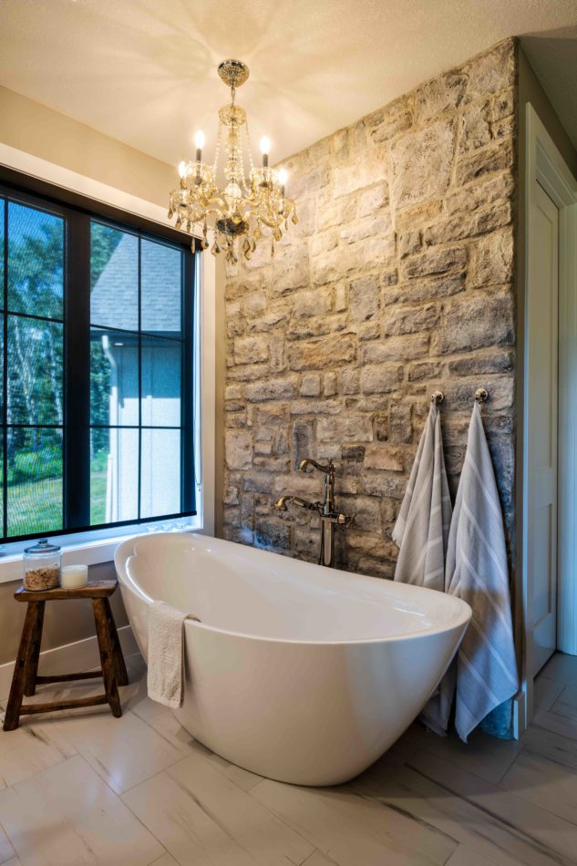 Ensuite free-standing tub with stone wall and chandelier 