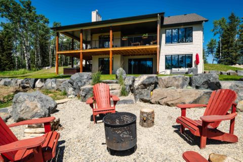 Rear exterior fo modern farmhouse bungalow with fire pit and red muskoka chairs