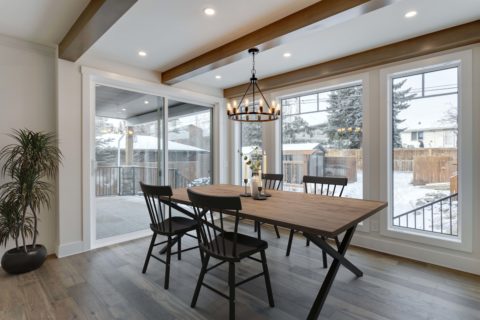 Calgary infill custom home builder. Farmhouse style dining room with rectangular table and three fir ceiling beams. Large windows looking into the backyard. 