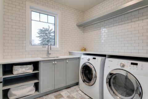 Laundry room with full height tile. Calgary, Alberta custom home builder. Blue cabinets and quartz countertops.