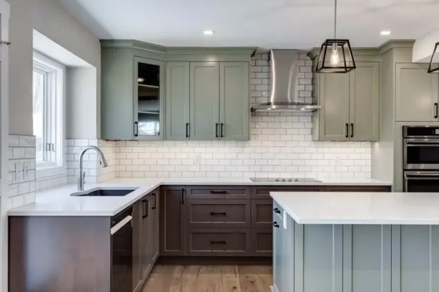 Custom Calgary kitchen featuring two-tone beveled Shaker cabinetry in Louisburg Green and custom rich brown stain with matte black hardware, sink with Blanco Silgranit sink and pendant lighting over island
