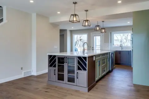 Closeup of Calgary custom kitchen island with prep sink featuring two-tone beveled Shaker cabinets in Louisburg Green and custom rich brown stain and glass front cabinets at end