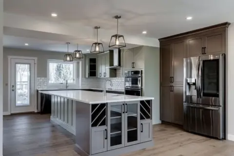 Wide angle view of Calgary kitchen with custom two-tone beveled Shaker cabinets in Louisburg Green and custom rich brown stain, glass front cabinets at end of large island with prep sink