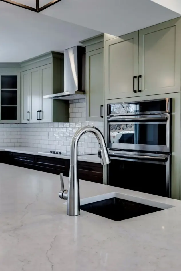 Closeup of prep sink in island of Custom Calgary kitchen featuring two-tone beveled Shaker cabinetry in Louisburg Green and custom rich brown stain with matte black hardware