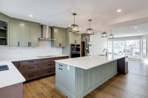 Custom Calgary kitchen featuring two-tone beveled Shaker cabinetry in Louisburg Green and custom rich brown stain with matte black hardware, Blanco Silgranit prep sink and pendant lighting over island