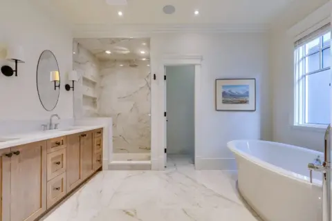 Primary ensuite with custom vanity, quartz countertops, frameless glass shower, and freestanding tub