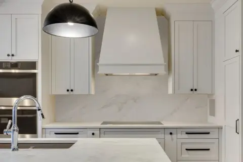 View from island to custom white Shaker inset cabinetry and hood fan