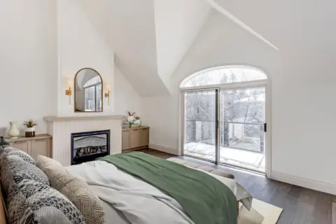 Vaulted ceiling bedroom with gas fireplace, custom built-in cabinetry, and patio doors to balcony