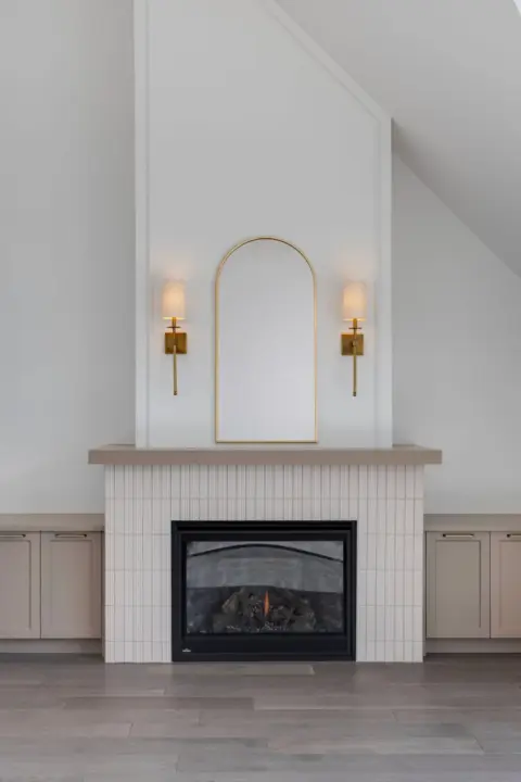 Closeup of tiled fireplace and mantle with sconce lighting and flanked by custom built-in cabinetry