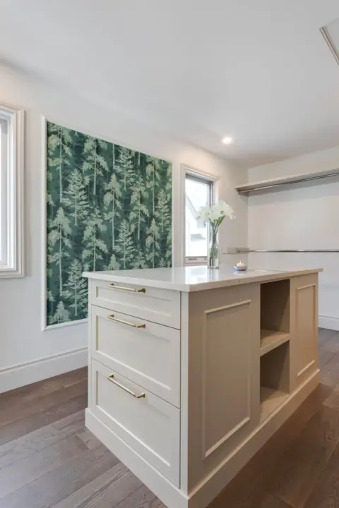 Dream walk-in closet with central island, ample storage, and wallpaper accent