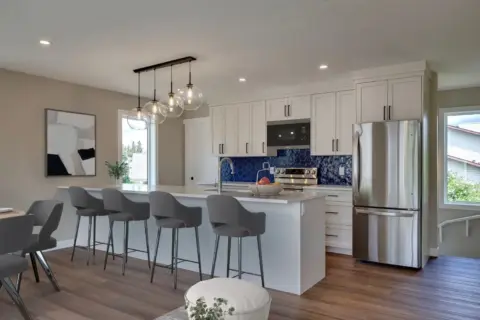Kitchen in light-filled carriage home with neutral coloured Shaker cabinetry, chrome tap, black lighting and hardware, and rich cobalt blue hex tile backsplash.