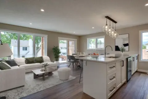 View of main living area in a garage carriage home including flush eating bar, living and dining areas, with windows on two sides and patio doors out to a covered deck.