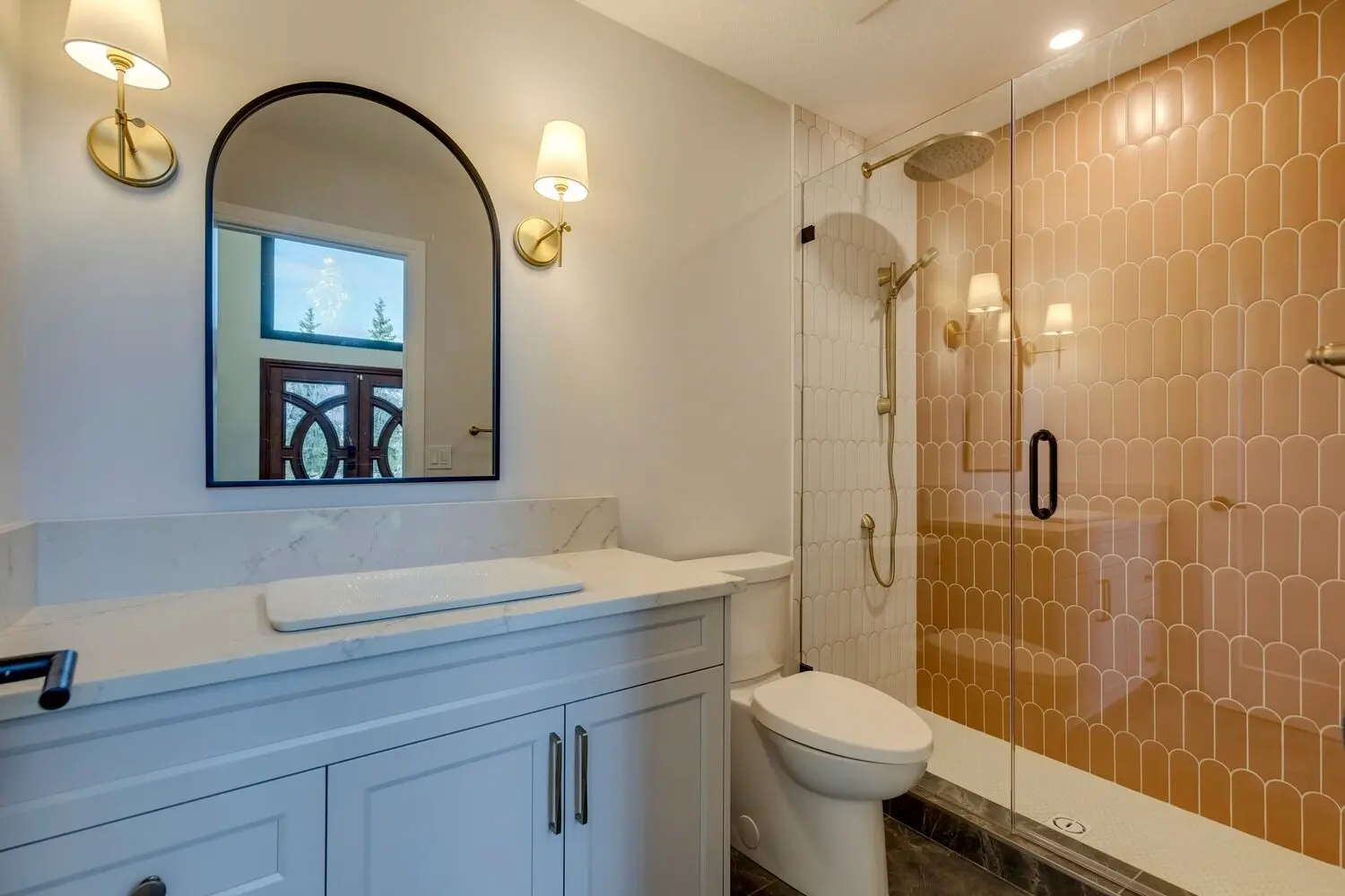 Bathroom in renovated Rocky View County home featuring uniquely shaped terracotta coloured tile in the shower accented by brass and black hardware and fixtures