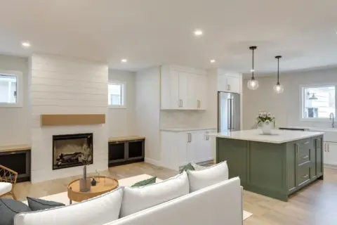 Open concept living room with shiplap fireplace wall and kitchen featuring bold green island and white Shaker cabinetry with brushed gold hardware in Calgary home remodeled by Melanson Homes