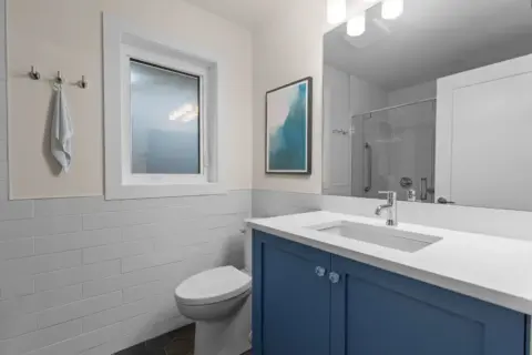 Bathroom with bright blue custom cabinetry and quartz countertop in expanded and fully renovated Charleswood home
